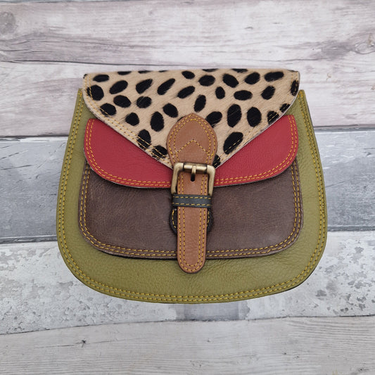 Lalita is a saddleback style bag with a front buckle. Made from leather off-cuts she is shown here in a mix of green, brown and red colours and finished with a textured panel in a spotty print.