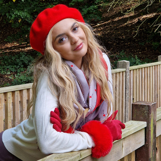 Young woman wearing a red beret with matching gloves and a grey and red scarf.