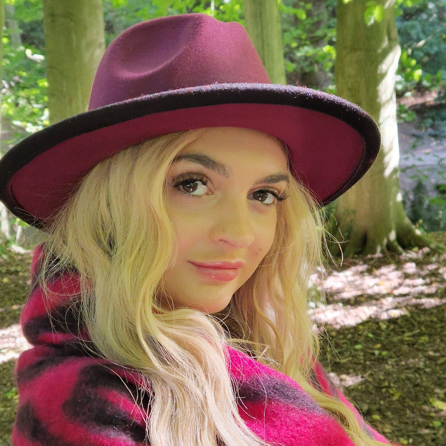 Young woman wearing a black and burgundy Fedora hat and matching pink and black zebra print scarf.