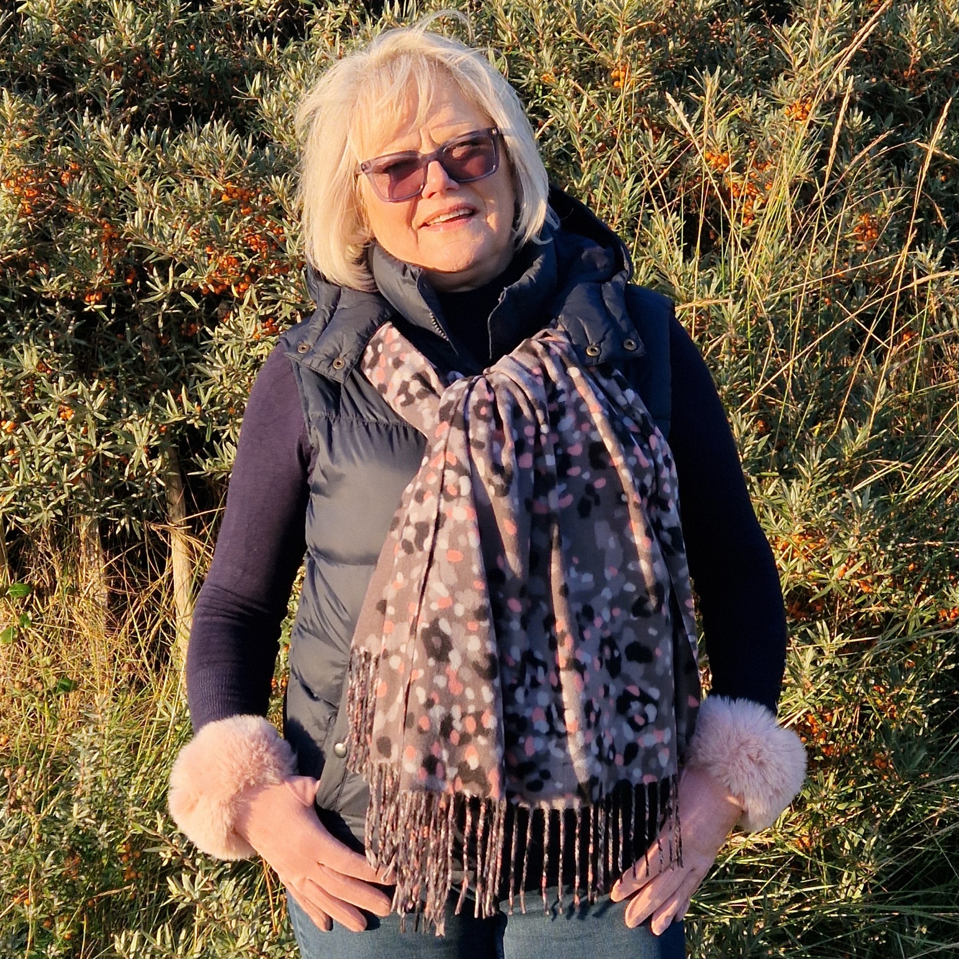 Lady wearing a winter scarf in grey, pink and black pattern with matching pale pink gloves with a faux fur cuff.