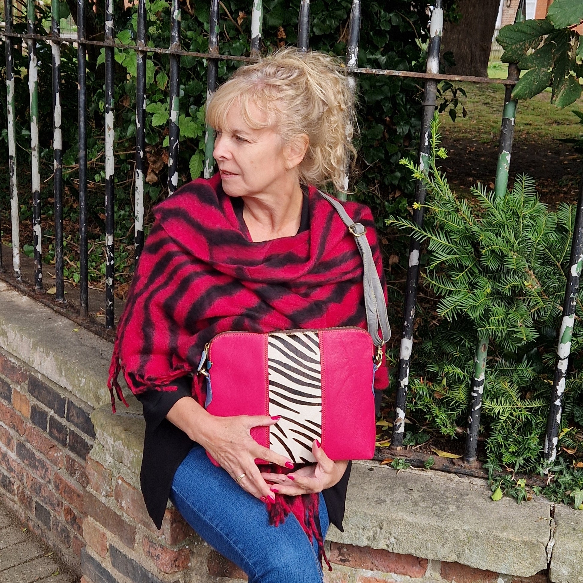 Lady wearing a large pink and black zebra print blanket scarf and pink and zebra print bag with crossbody strap.