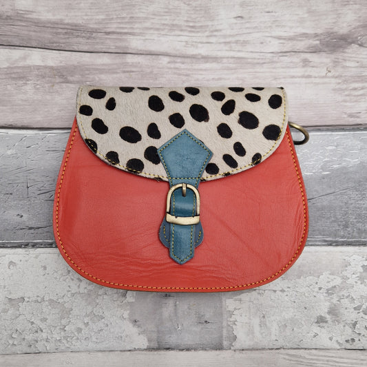 Leather saddlebag shaped bag with a bright orange front and a textured panel of spotty print.