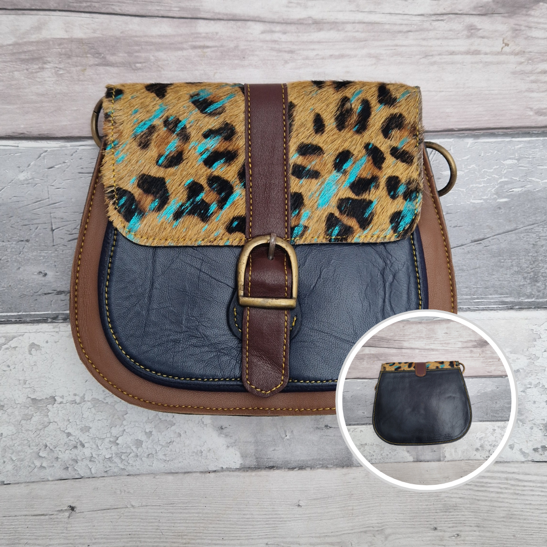 All leather saddlebag style ladies bag in tan brown and navy with a textured panel of leopard print splattered with metallic blue splashes. Brass buckle closer.