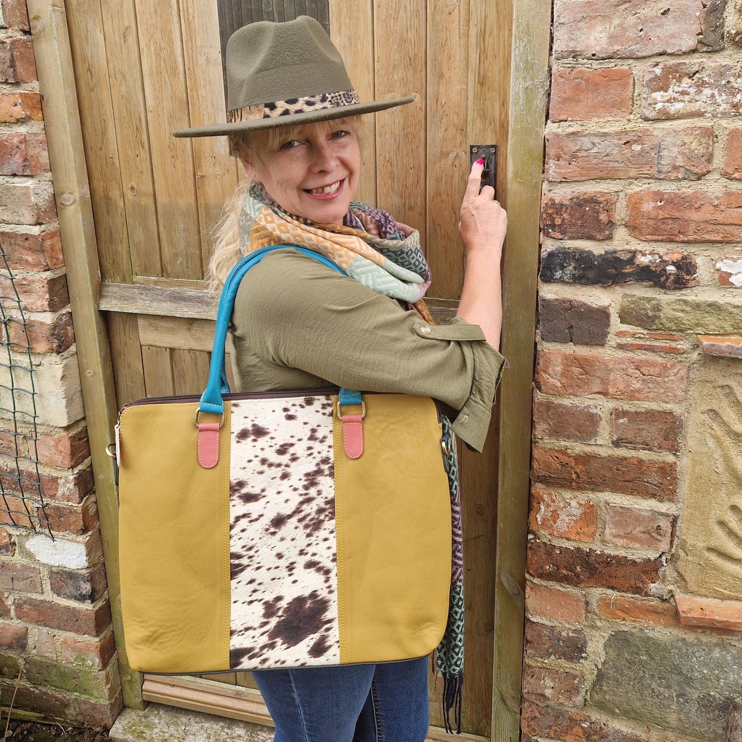 Lady carrying a mustard coloured leather tote bag with a panel of textured cow hide running down the centre of the front panel.