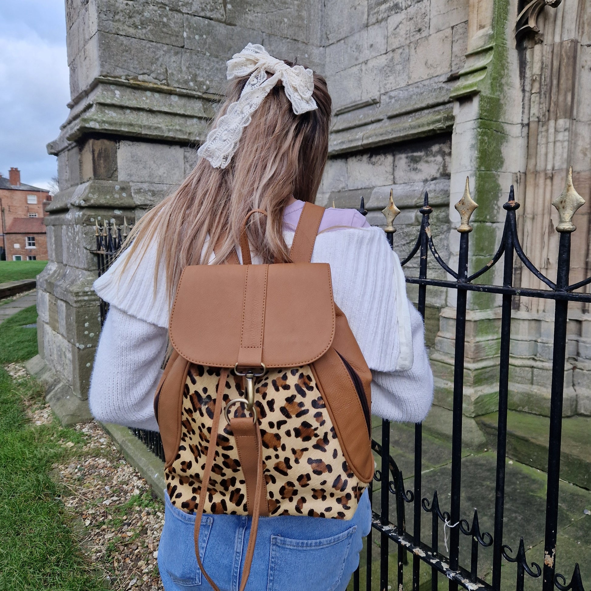 Young woman wearing a Tan leather back pack with textured panels of leopard print.