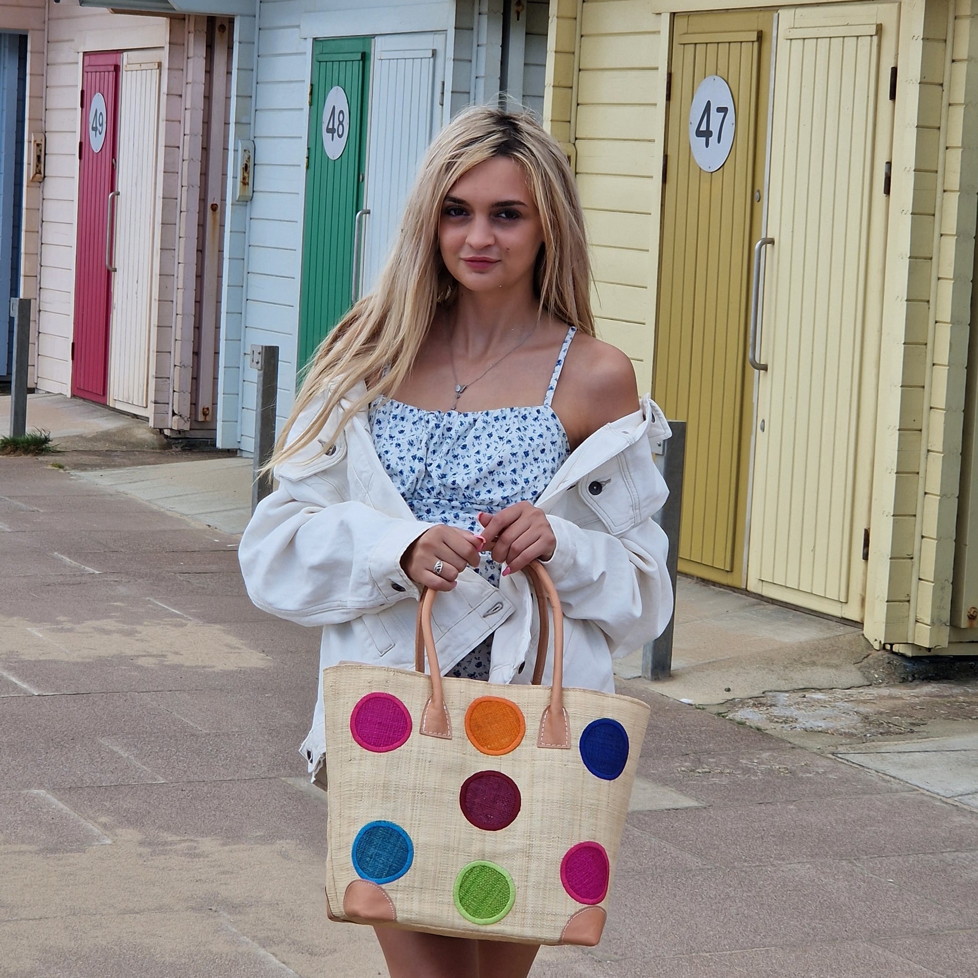 Young woman carrying a natural coloured raffia basket with brightly coloured spots on.