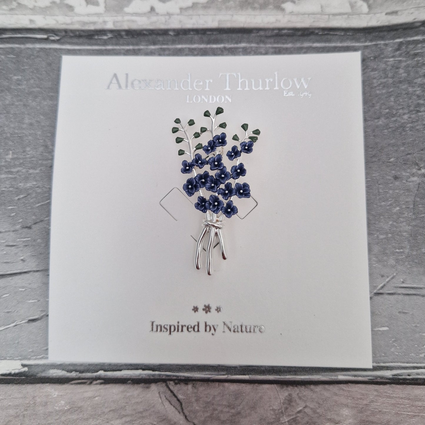 Hand painted inky blue enamel and silver tone brooch featuring 3 tall delphinium flower stems bunched together. Shown on display card.