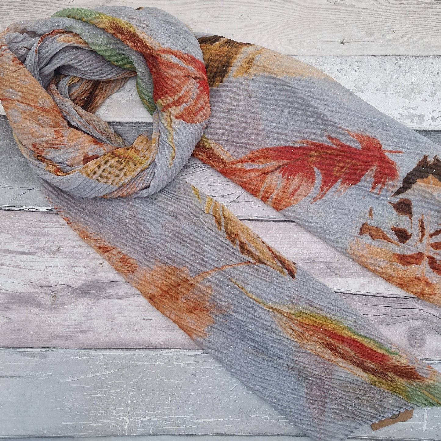 Crinkle effect pale grey scarf decorated with feathers in orange, green and brown.