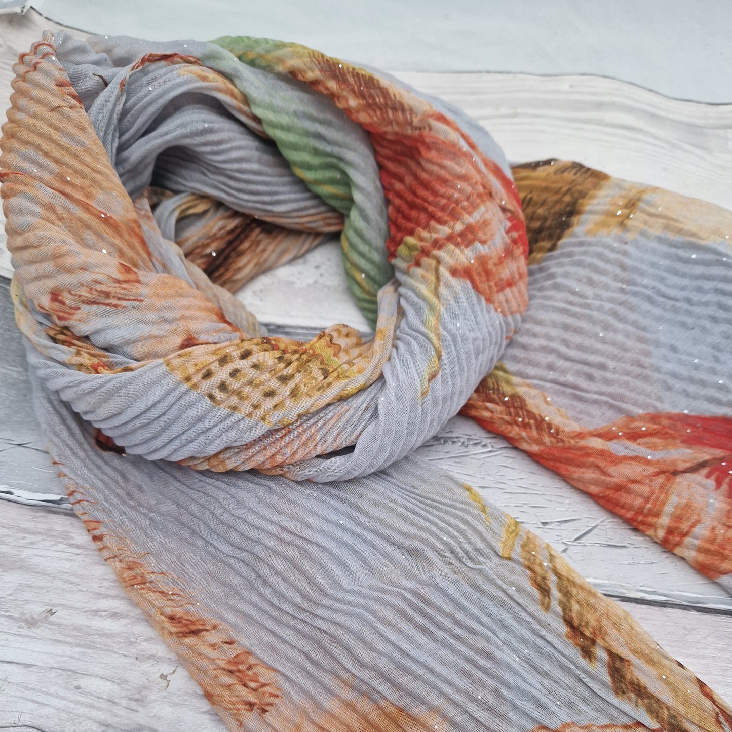 Crinkle effect pale grey scarf decorated with feathers in orange, green and brown.