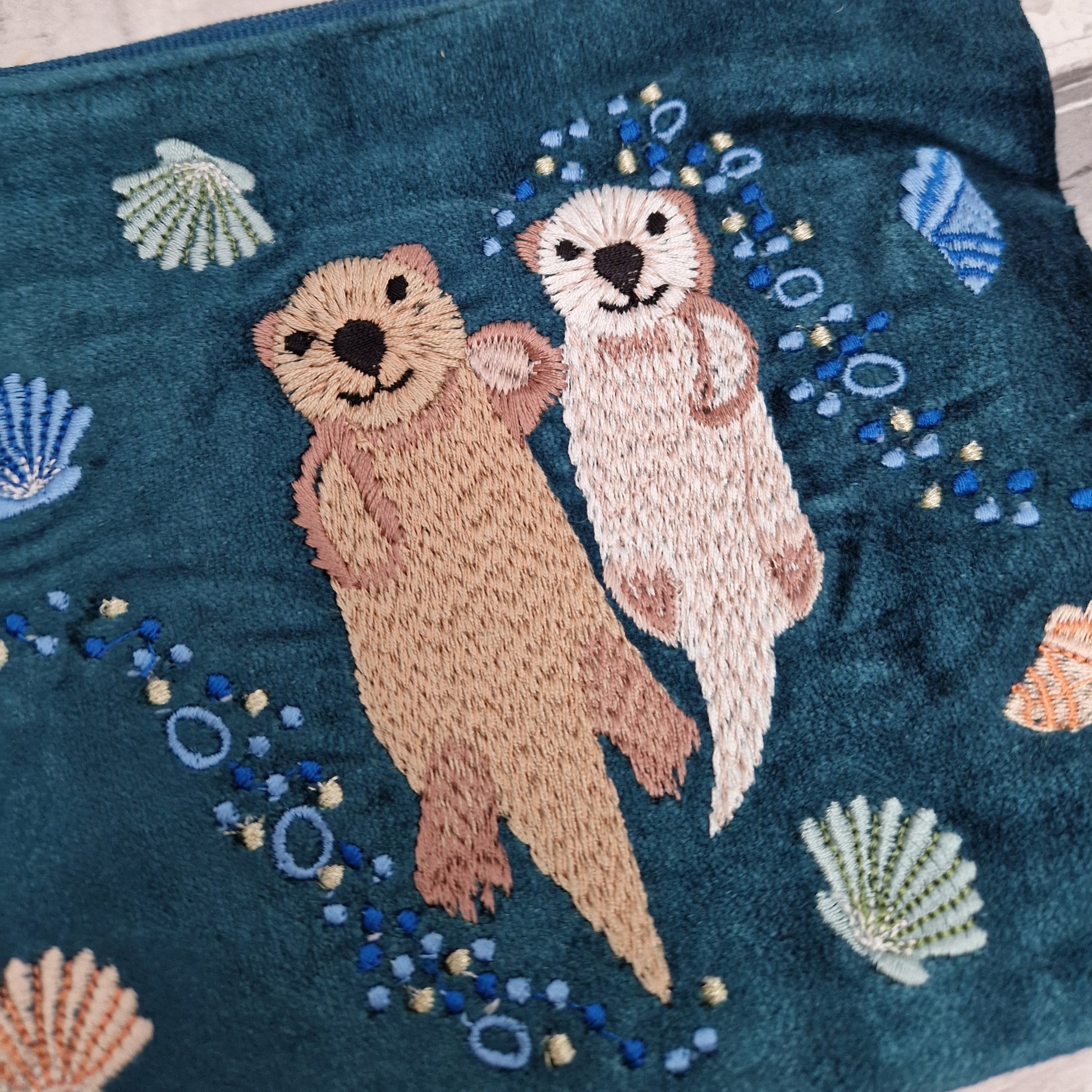 Close up view of turquoise velvet pouch with Otters and sea shells.