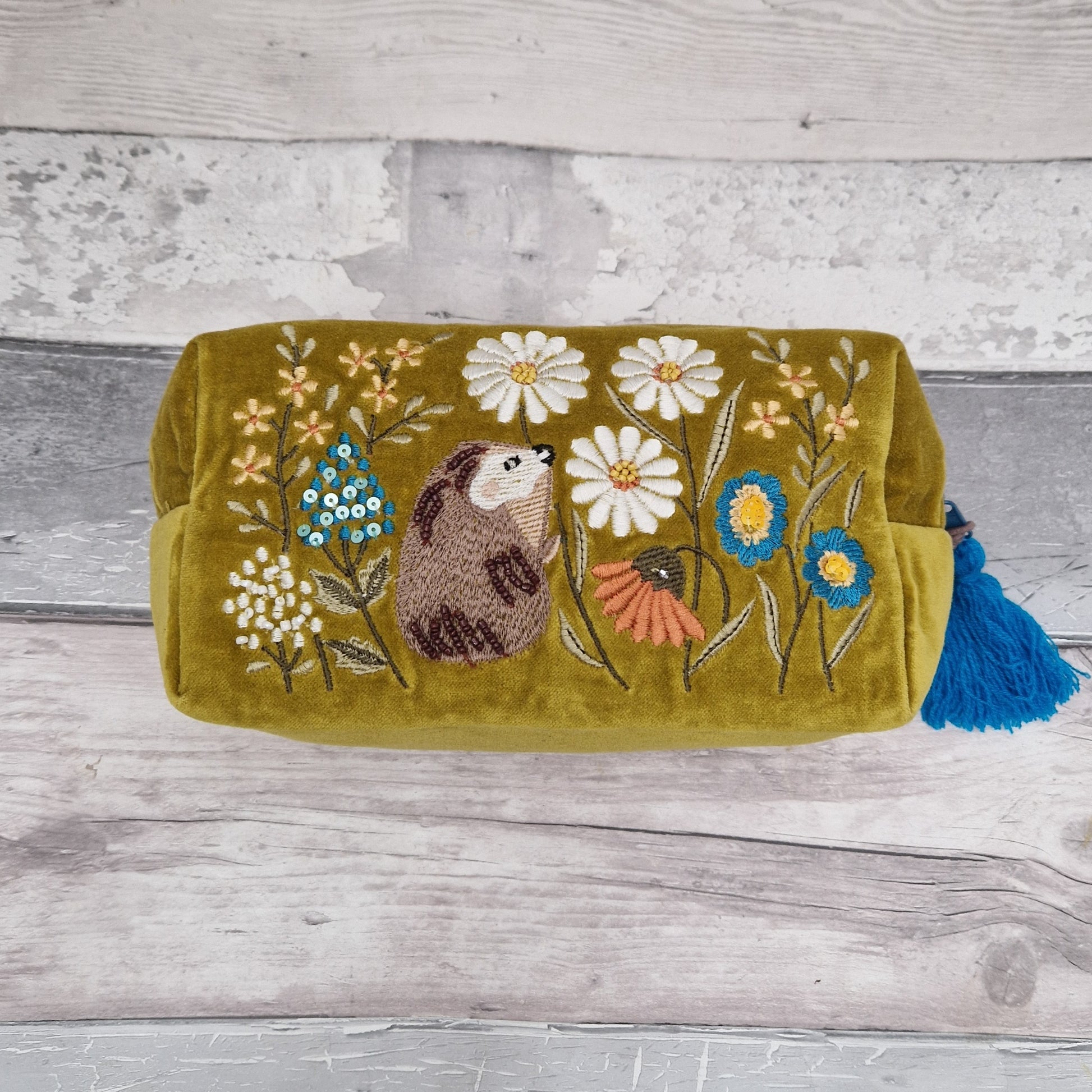 A Mustard colored velvet wash bag. Decorated with hand embroidery, sequins and beads, depicting a hedgehog in a wild flower meadow.