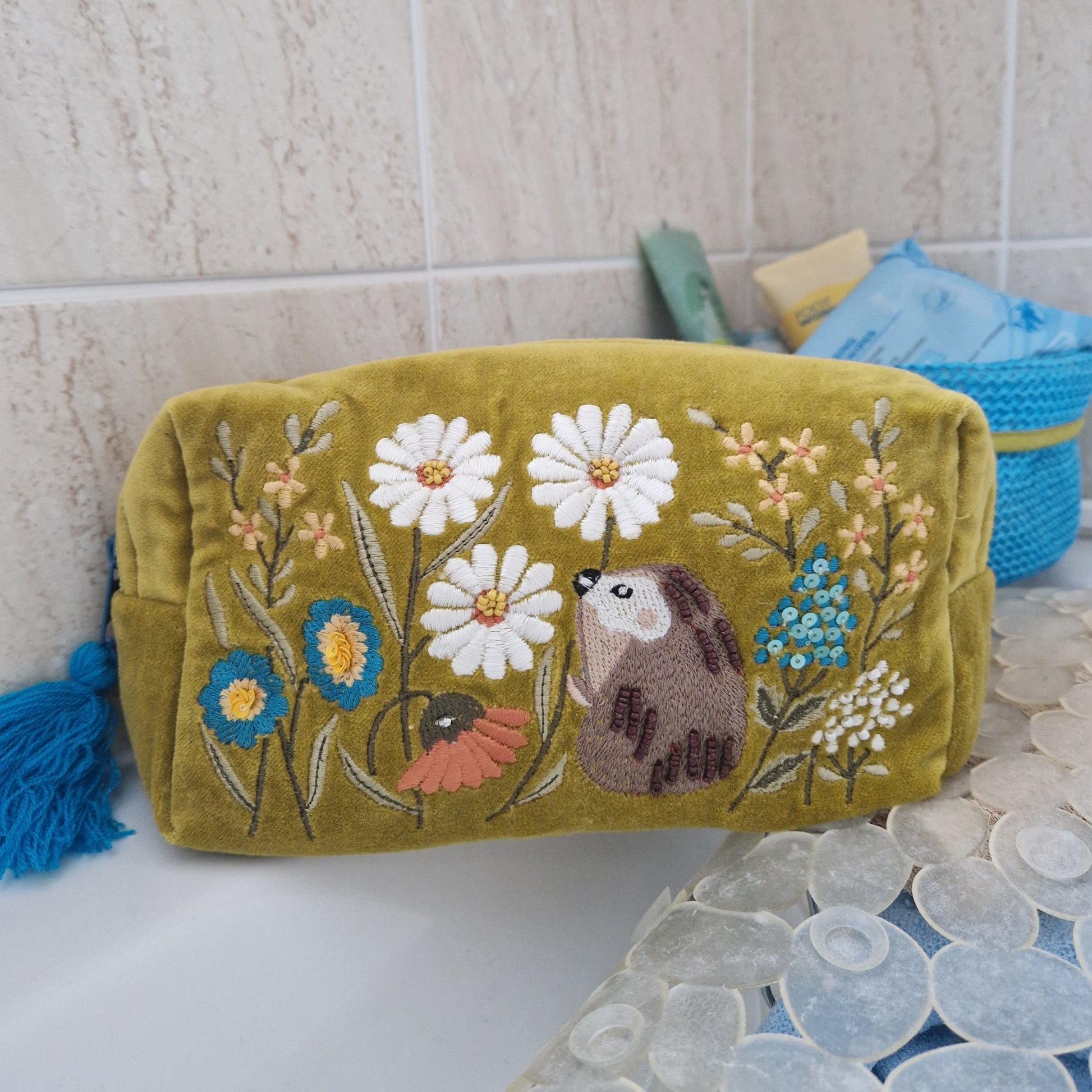 A Mustard colored velvet wash bag. Decorated with hand embroidery, sequins and beads, depicting a hedgehog in a wild flower meadow.