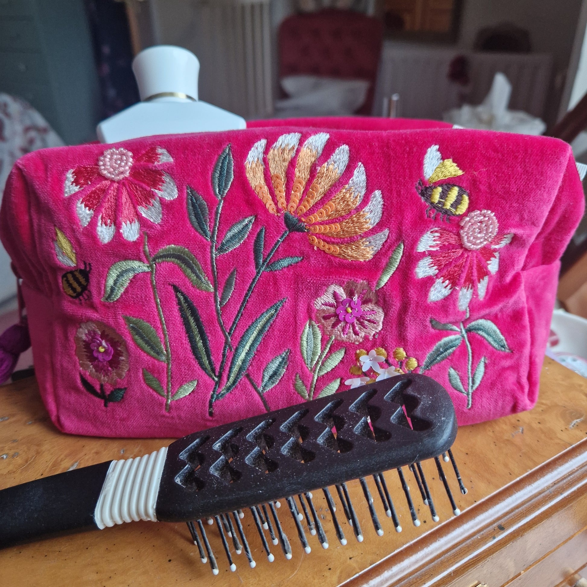 A hot pink velvet washbag. Decorated with embroidery, hand sewn sequins and beads. Depicting a flower garden with bumble bees. 