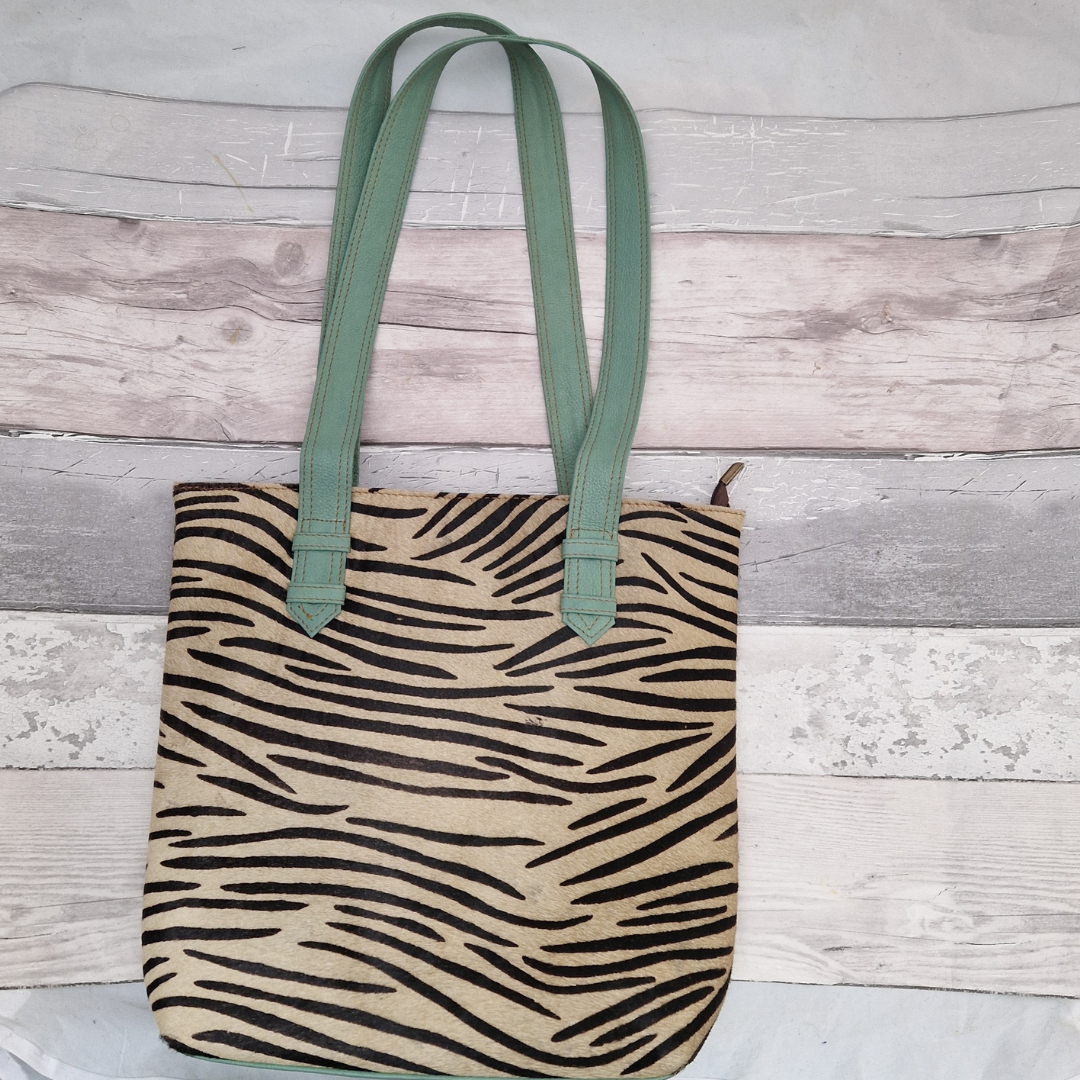 All leather tote bag made with textured panels decorated in Zebra print. Long handles in aqua blue leather.