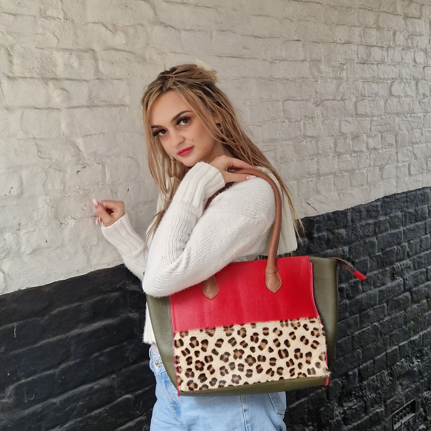 Young woman modelling long handled handbag on her shoulder. Bag is leather, made up of brightly coloured panels including one texture panel of leopard print.