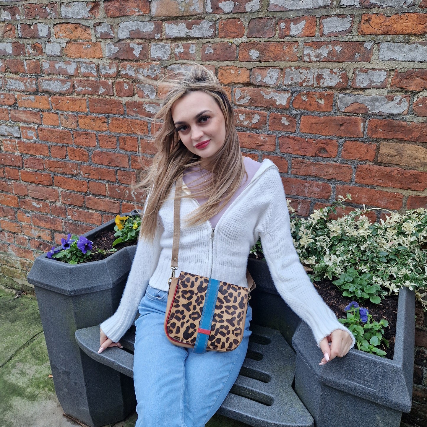 Young woman wearing a messenger style bag across her body. Bag is multicoloured with a large front panel in Leopard print.