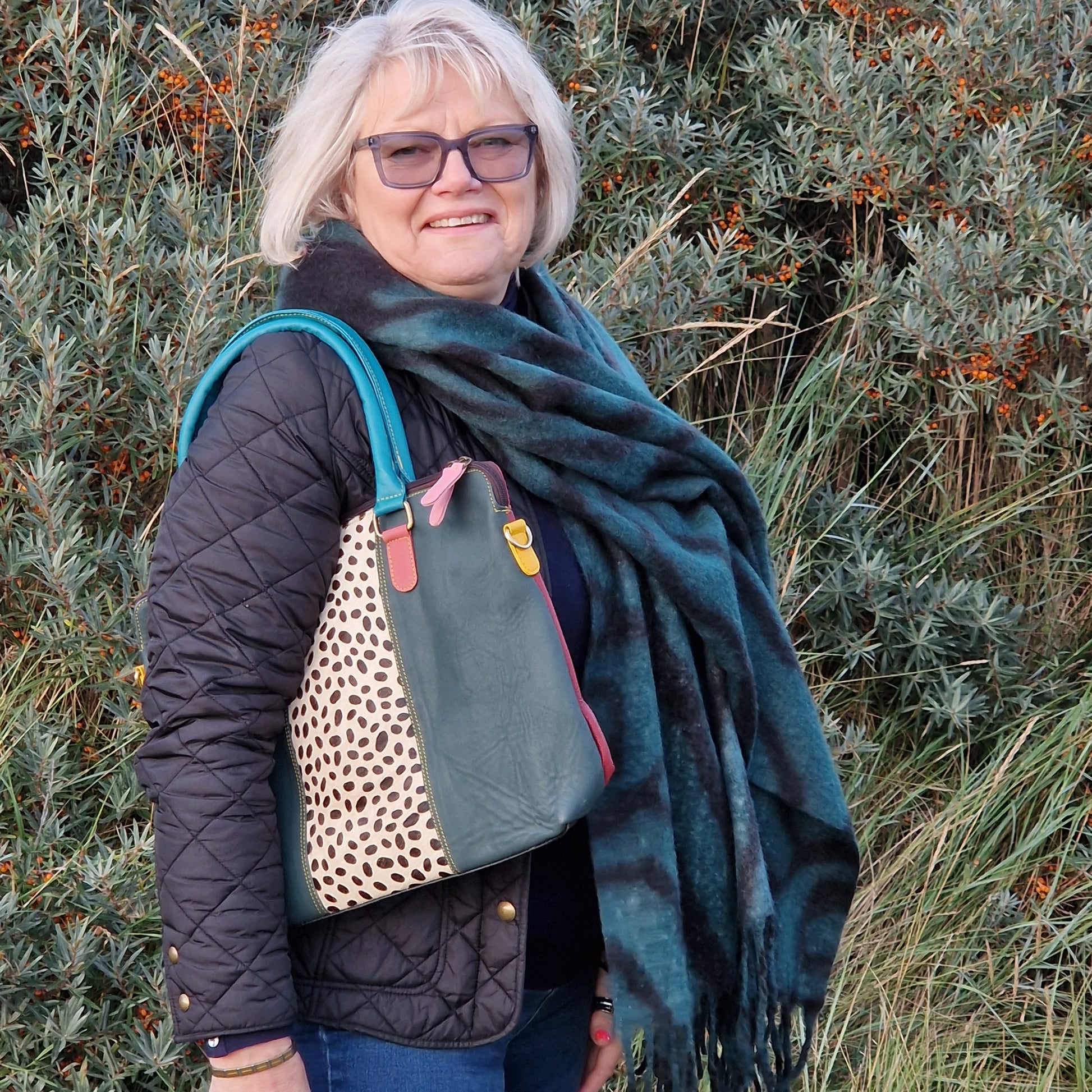 Lady wearing a green and blanket blanket scarf with a Zebra print and carrying a leather tote bag in matching green.